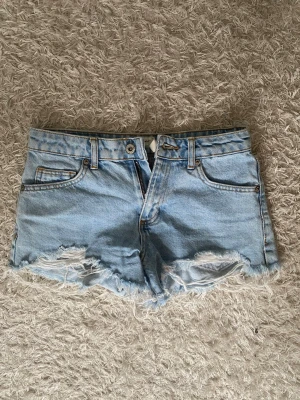 Ljusblå jeansshorts med fransig kant - Säljer ett par ljusblå jeansshorts från Suite Benedict med fransig kant och slitna detaljer framtill. Klassisk femficksmodell med knapp och dragkedja. 