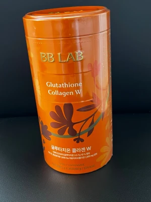 BB Lab Glutathione Collagen W - BB Lab Glutathione Collagen W är ett kosttillskott för skönhet, förpackat i en orange cylinderformad burk med blommönster. Produkten innehåller kollagen och glutathion och är avsedd att stödja hudens elasticitet och lyster. 