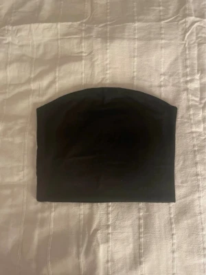 Svart tubtopp från Bik Bok - En enkel och stilren svart tubtopp från Bik Bok i storlek M. Toppen är axelbandslös och har en klassisk bandeauform som sitter tight mot kroppen. Perfekt att matcha med höga jeans eller kjol för en clean look.