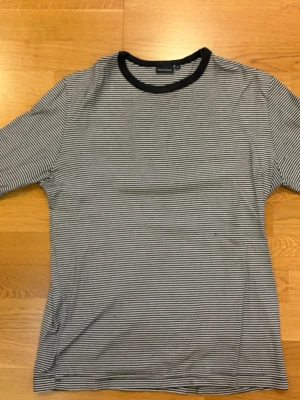 Randig svartvit t-shirt Weekday - Säljer en svartvit randig t-shirt från Weekday med smala horisontella ränder och svart ribbad krage. Klassisk passform och korta ärmar, perfekt till jeans eller kjol. Materialet känns mjukt och skönt, troligen bomull eller bomullsblandning.