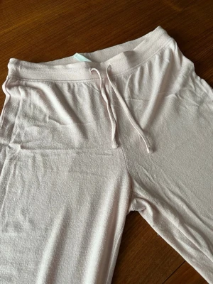 Ljusrosa mjukisbyxor med dragsko - Ljusrosa mjukisbyxor med elastisk midja och dragsko. Byxorna har raka ben och är gjorda i ett mjukt och bekvämt material som passar perfekt för chill dagar. Enkel design utan logga eller mönster.