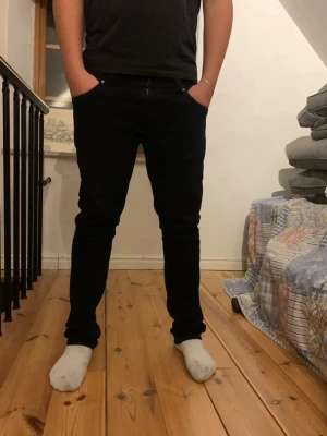 Svarta slim fit jeans från nudie - Säljer ett par svarta slim fit jeans med klassisk femficksdesign och normal midja. Jeansen har smal passform hela vägen ner och är tillverkade i ett stretchigt material för extra komfort. Perfekta till en enkel t-shirt eller hoodie. 