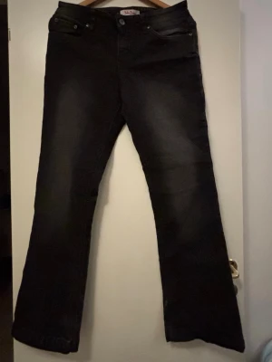 Svarta bootcut jeans John Baner - Snygga svarta jeans från John Baner med bootcut-modell och klassisk femficksdesign. Jeansen har subtila slitningar och är gjorda i ett mjukt denimtyg som sitter skönt. Perfekta för dig som gillar en tidlös look med lite extra vidd vid bensluten.