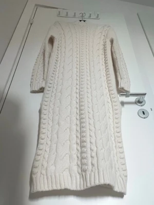 Mango Vit stickad långklänning kabelmönster, XS - Mysig vit stickad långklänning med klassiskt kabelstickat mönster och ribbade muddar. Klänningen har lång ärm och är perfekt för kyligare dagar. Passformen är normal och materialet känns mjukt och varmt. Mango, XS