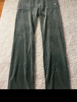 Grå velourbyxor från Juicy Couture - Säljer ett par grå mjukisbyxor i velour från Juicy Couture. Byxorna har raka ben, bred resår i midjan med dragsko och stora fickor fram. Klassisk Juicy Couture-logga broderad på ena fickan. Perfekta för en chill och trendig look.