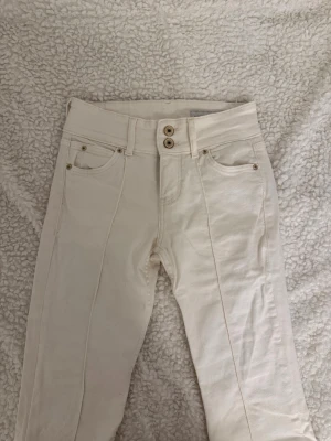 Vita raka jeans från Bershka - Säljer ett par vita jeans från Bershka . Jeansen har dubbla knappar i midjan, klassiska fem fickor och dekorativa sömmar framtill. Perfekta för en clean och fräsch look till vardags eller när du vill sticka ut lite extra.