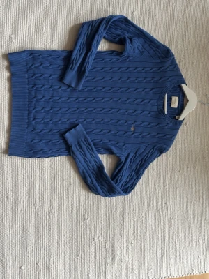 Blå kabelstickad tröja från Gant - Snygg blå kabelstickad tröja från Gant med rund halsringning och ribbade muddar. Tröjan har ett diskret Gant-broderi på bröstet och är tillverkad i mjukt material som passar perfekt till lager på lager. Klassisk och tidlös design. Nypris:1600kr, hör av er med minsta lilla fundering!