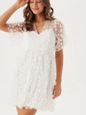 Studentklänning - Superfin vit kortklänning med blommigt mönster och spetsdetaljer. Klänningen har v-ringning och transparenta kortärmar med blommor. Perfekt stundentklänning! Nypris 999kr