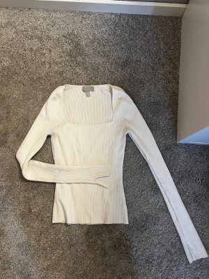 Vit ribbad topp från H&M - Säljer en vit ribbad topp från H&M med lång ärm och fyrkantig ringning. Toppen är tight i modellen och har en stilren look som passar perfekt till jeans eller kjol. Materialet är mjukt och stretchigt för en bekväm passform.