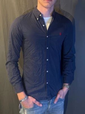 Mörkblå skjorta från Ralph Lauren - Snygg mörkblå skjorta från Ralph Lauren. Skjortan sitter i slimfit så sitter väldigt bra runt kroppen. Modellen är 190cm och väger 80kg. Skriv om du har frågor 🥰