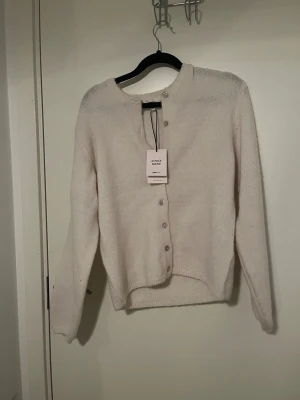 Stickad kofta  - Mysig ljusbeige kofta från Arket i alpaca blend. Koftan har rund halsringning, långa ärmar och knappar framtill. Perfekt för lager på lager och enkel att matcha med olika outfits.