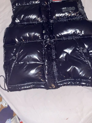 Svart glansig dunväst från HUGO - Säljer min svart dunväst från HUGO som går och använda till inprincip allt kom med buddd den e helt ny har aldrig använt den