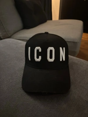 Svart ICON keps från Dsquared2 - Säljer en svart keps från Dsquared2 med stor vit brodyrtext 'ICON' framtill. Klassisk böjd skärm och justerbar baksida. Tillverkad i bomull och har en modern streetwear-look som sticker ut.