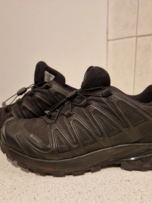 Svarta Salomon XA Pro 3D sneakers - Svarta Salomon XA Pro 3D GTX sneakers med vattentätt Gore-Tex-material, robust sula med Contagrip och snabbsnörning. Perfekta för utomhusaktiviteter och äventyr. Snygg sportig design med diskreta detaljer och bekväm passform. Är i storlek 40 herr och är använda några fåtal gånger. 