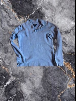 Ljusblå halvzip från Polo Ralph Lauren - Ljusblå långärmad tröja från Polo Ralph Lauren med halvzip och broderad logga på bröstet. Tröjan har en ribbad struktur och hög krage som kan bäras öppen eller stängd. Perfekt för en avslappnad men ändå stilren look. Finns tyvär ett litet hål på ryggen men inget som man märker. De står L i den men de är L i barnstorlekar så dem passar ungefär någon som är melöan 158-165