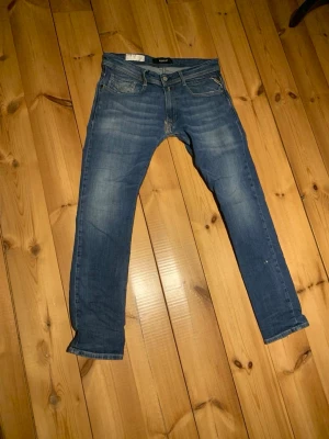 Blå slim fit replay jeans - Säljer ett par blå slim fit jeans från  med klassisk femficksdesign och dragkedjegylf. Jeansen har slitningar och kontrastsömmar för en cool look. Perfekta till vardagsstilen och passar till det mesta. Det är ett sytt hål vid gylfen.