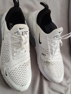 Nike Air Max 270 vita sneakers - Nike Air Max 270 sneakers i vitt med svarta detaljer och synlig Air-enhet i hälen. Ovandelen är i mesh för bra ventilation och har klassisk Nike-logga på sidan och plösen. Snygg och sportig design med snörning och låg profil.    Pris kan diskuteras