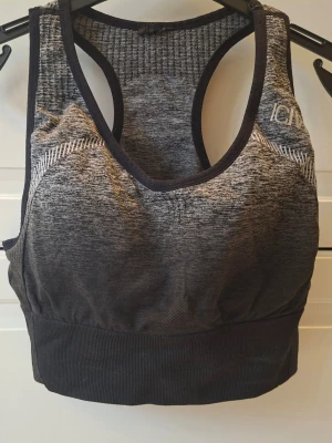 Grå-svart sport-bh från ICANIWILL. Seamless sports bra. - Sport-bh i gråmelerat och svart med brottarrygg och bred resår. Sömlös design i stretchigt funktionsmaterial som andas. Diskret ICANIWILL-logga på axeln och snygga stickade detaljer framtill och baktill.