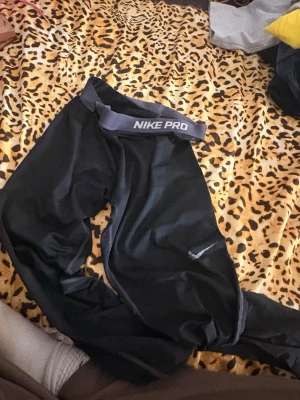 Svarta Nike Pro träningstights - Svarta Nike Pro träningstights med elastisk midja och tydlig Nike Pro-logga. Tightsen har en åtsittande passform och är tillverkade i ett stretchigt funktionsmaterial som passar perfekt för träning och sportaktiviteter.