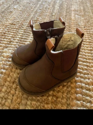 Bruna Chelsea boots från thisistheseboots - Snygga bruna Chelsea boots med dragkedja på sidan och elastiska partier. Boots i läderimitation med mjukt, ljust foder och praktiska dragflikar fram och bak. Perfekta för en stilren look under höst och vinter.