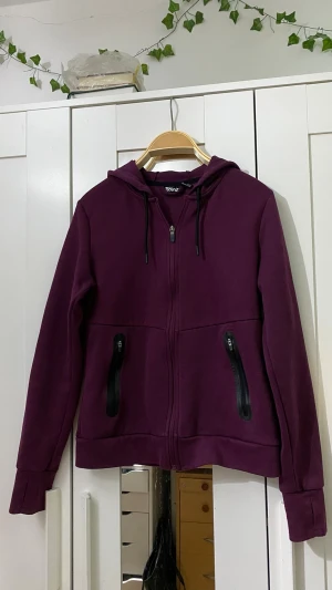 Lila hoodie med dragkedja - Snygg lila hoodie från Divided med hel dragkedja framtill och två svarta dragkedjeförsedda fickor. Modellen har huva med dragsko och ribbade muddar vid ärmslut och nederkant. Perfekt för en chill och avslappnad stil.