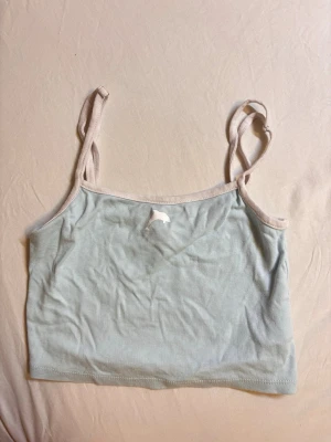 Ljusblå cropped linne med smala band - Säljer ett ljusblått cropped linne med tunna axelband och ljusbeige kant. Toppen har en enkel och stilren design, perfekt för layering. Materialet känns mjukt och stretchigt, troligen bomull eller bomullsblandning. Ingen synlig logga eller märke.