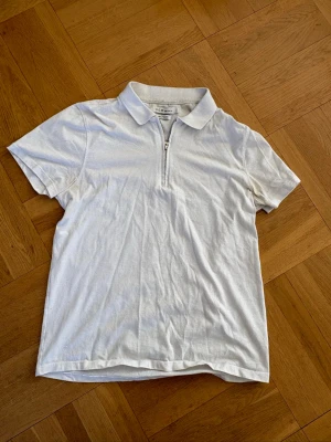 Vit t-shirt med krage och dragkedja - Vit t-shirt från S.C.W med klassisk krage och halv dragkedja framtill. T-shirten är kortärmad och har en stilren look som passar perfekt till jeans eller shorts. Tillverkad i mjuk bomull för en skön känsla hela dagen.