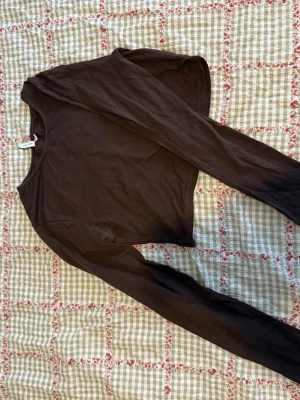 Brun långärmad topp från Nelly  - Mörkbrun långärmad topp från NLY Trend. Enkel och stilren design med rund halsringning och croppad passform. 