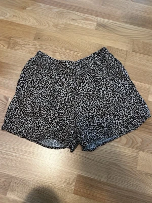 Leopardmönstrade shorts med resår - Snygga shorts med leopardmönster i svart och beige. De har en avslappnad passform och elastisk midja för extra komfort. Perfekta för varma dagar när du vill sticka ut lite extra. Har även fickor fram på båda sidor.