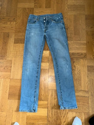 Blå raka jeans från Levi's - Snygga blå jeans från Levi's i rak modell med klassisk femficksdesign. Jeansen har en lätt tvättad look och små slitningar för en trendig känsla. Tillverkade i 94% bomull och 6% elastan för skön stretch och passform.