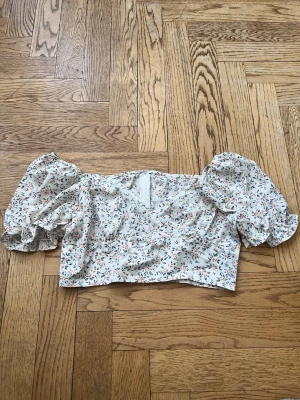 Blommig croppad blus med puffärm - Supersöt croppad blus med blommigt mönster i ljusa färger och stora puffärmar. V-ringad framtill och dragkedja i ryggen. Perfekt för dig som vill ha en romantisk och trendig topp till sommaren.