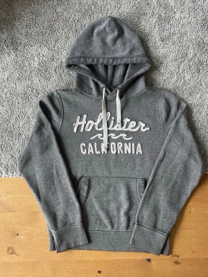 Grå hoodie från Hollister - Grå Hollister hoodie i storlek L säljes. I mycket bra skick och utan defekter. Bekväm och stilren hoodie med Hollister California tryck framtill.  ✅ Storlek L ✅ Mycket bra skick ✅ Inga defekter ✅ Snabb frakt  Hör gärna av er vid frågor eller om ni vill ha fler bilder!