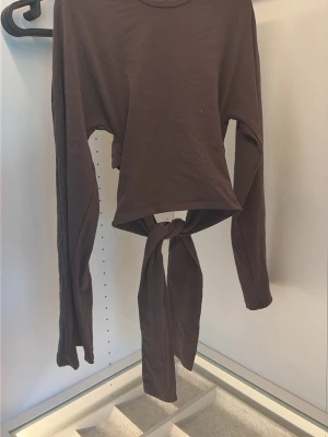 Brun långärmad topp med knyt - Säljer en brun långärmad topp från 157 i storlek XS. Toppen har ett snyggt knyt framtill som ger en trendig look och är tillverkad i mjukt bomullsmaterial. Perfekt att styla med höga jeans eller kjol.