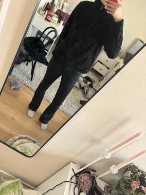 Svart teddyjacka med dragkedja - Mysig svart teddyjacka med hög krage och hel dragkedja framtill. Jackan har en fluffig och mjuk yta som ger en avslappnad och trendig look. Perfekt för kyliga dagar när du vill vara både varm och snygg.