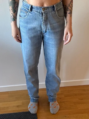 Ljusblå raka jeans med hög midja - Säljer ett par ljusblå jeans med rak passform och hög midja. Jeansen har klassiska fem fickor, bälteshällor och stängs med knapp och dragkedja. Perfekta för en avslappnad och trendig look.