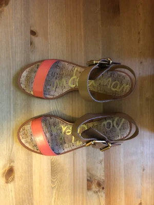 Sandaler med korksula - Snygga sandaler i äkta läder med bred rem i korallrosa framtill och beige rem runt vristen med guldfärgat spänne. Sulan har korkmönster och logga i gult. Perfekta för sommaren och ger en fräsch look till din outfit.