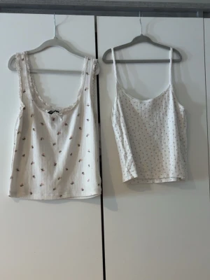 Två blommiga linnetoppar från H&M Divided - Säljer två söta linnetoppar från H&M Divided i storlek S. Båda är vita med små blommiga mönster, en har spetskant och rosett vid urringningen. Perfekta att styla med jeans eller kjol för en chill look.