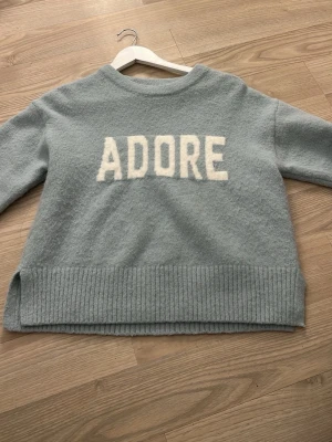  stickad tröja  - Stickad blågrön tröja med text Adore på. Använd fåtal gånger. 