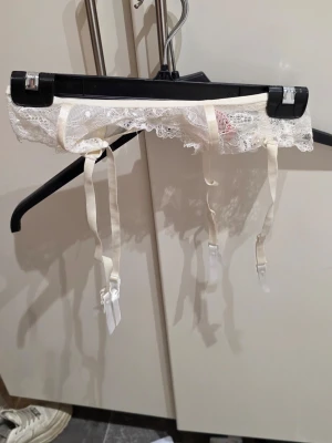 Romantisk spets-strumpebandshållare Hunkemöller (Stl M) Garter Belt - Säljer en jättevacker strumpebandshållare i vit spets från välkända Hunkemöller. Endast använd vid ett tillfälle (bröllop) och är i absolut nyskick!  Perfekt för bruden, till festliga tillfällen eller för att addera lite vardagslyx. Den har justerbara band och vackra detaljer i spetsen.  ✨ Produktinfo: Märke: Hunkemöller Storlek: Medium (M) Färg: Vit / Ivory Skick: Nyskick (använd en gång) Detaljer: Justerbara remmar, klassiskt knäppe bak. 