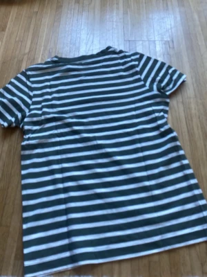 Randig t-shirt i grönt och vitt - Snygg t-shirt med gröna och vita horisontella ränder. Klassisk passform med korta ärmar och rund halsringning. Perfekt för en avslappnad stil och enkel att matcha med jeans eller shorts.