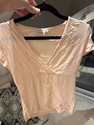 Ljus rosa omlottopp från Nelly - Snygg ljus rosa omlottopp från Nelly med korta ärmar och v-ringad hals. Endast använd ett fåtal gånger.