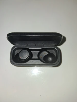 Svarta trådlösa in-ear hörlurar, Skullcandy - Säljer ett par svarta trådlösa in-ear hörlurar med laddningsetui. Hörlurarna har en minimalistisk design och är helt svarta med rundade former. Perfekta för musik, poddar eller samtal på språng. Laddningsetuiet är kompakt och lätt att ta med sig. missar bara höger sida poden