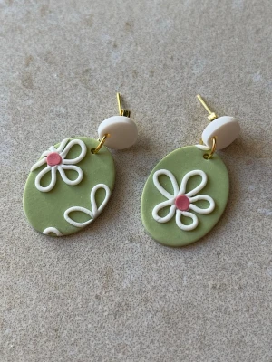 Handgjorda örhängen – gröna med blommor (3 cm) - Handgjorda örhängen i mjuk grön nyans med vita blommor och små rosa detaljer samt stilren vit topp. En lekfull men stilren design som passar både till vardag och finare tillfällen. Lätta att bära och bekväma i öronen. Varje par är unikt och gjort för hand. Längd: ca 3 cm. Säljs som par.
