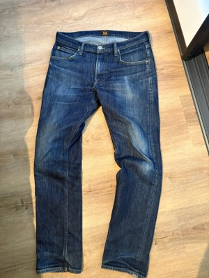 Blå jeans från Lee med raka ben - Snygga blå jeans från Lee med klassisk femficksdesign och raka ben. Strorlek w31 L32 Jeansen har en lätt tvättad look med subtila slitningar och gylf med knapp. Perfekta för en avslappnad stil och passar till det mesta. Kom med prisförslag 