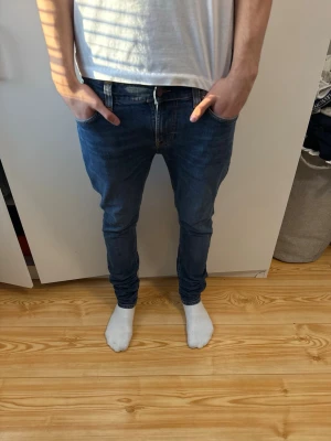 Blå slim fit Nudie Jeans  - Säljer ett par blå slim fit jeans från Nudie med klassiska bakfickor och snygga kontrastsömmar. Storlek W31/L32, nypris-1399kr mitt pris-500kr, nyskick använd max 2-3 gånger, pris kan diskuteras vid snabba affärer 