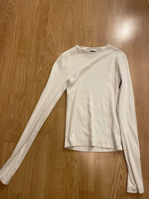 Vit ribbad långärmad topp Bik Bok - Snygg vit långärmad topp från Bik Bok i ribbat material. Modellen har rund halsringning och är figurnära, perfekt att styla med jeans eller kjol. Enkel och stilren design som passar till många olika looks.