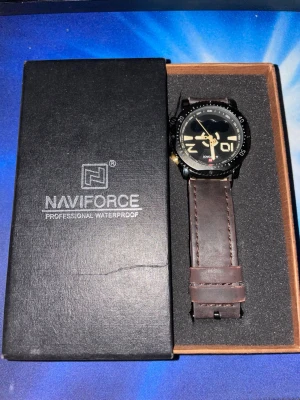 Naviforce klocka med brunt läderband - Snygg klocka från Naviforce med svart urtavla och stora siffror i guld. Klockan har ett robust brunt läderband och svart boett. Perfekt accessoar för dig som vill ha en stilren och sportig look.