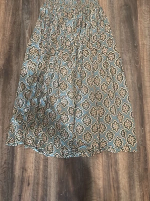 Mönstrad långkjol i grönt och beige - Säljer en flowy långkjol med grön och beige färg och ett snyggt orientaliskt mönster. Kjolen har en avslappnad passform och är gjord i ett lätt material som känns skönt mot huden. Perfekt för dig som gillar boho-stil och vill ha något unikt i garderoben.