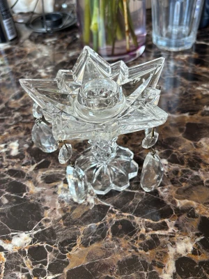 Kristall-ljusstake i stjärnform - Säljer en unik ljusstake i klar kristall med stjärnformad design och hängande prismor. Ljushållaren är placerad i mitten och hela ljusstaken har en glittrande, elegant look. Perfekt som dekoration på bordet eller i fönstret.