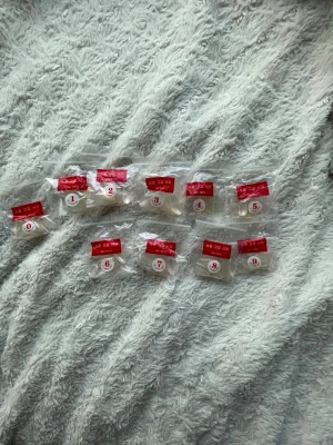 Klara långa press-on naglar - Säljer ett set med klara, långa press-on naglar i olika storlekar. Naglarna har en elegant, spetsig form och kommer i separata påsar märkta 0-9 för enkel sortering. Perfekta för att skapa egna designer eller använda som de är.